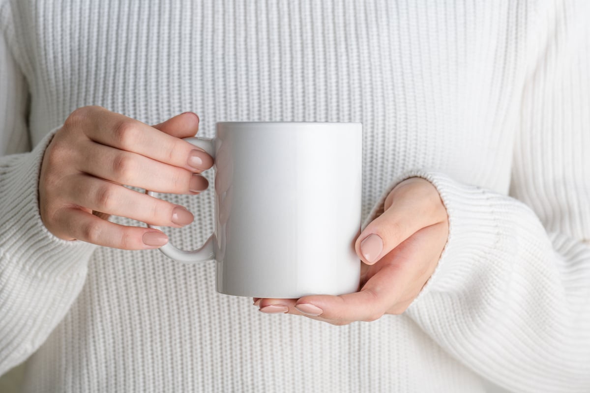 Girl in white sweater holding white porcelain coffee mug mock up, close up